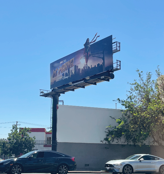 도로에 미즈 마블의 광고판이 세워져 있다. 왼쪽 기둥을 중심으로 세워진 대형 광고판이다.