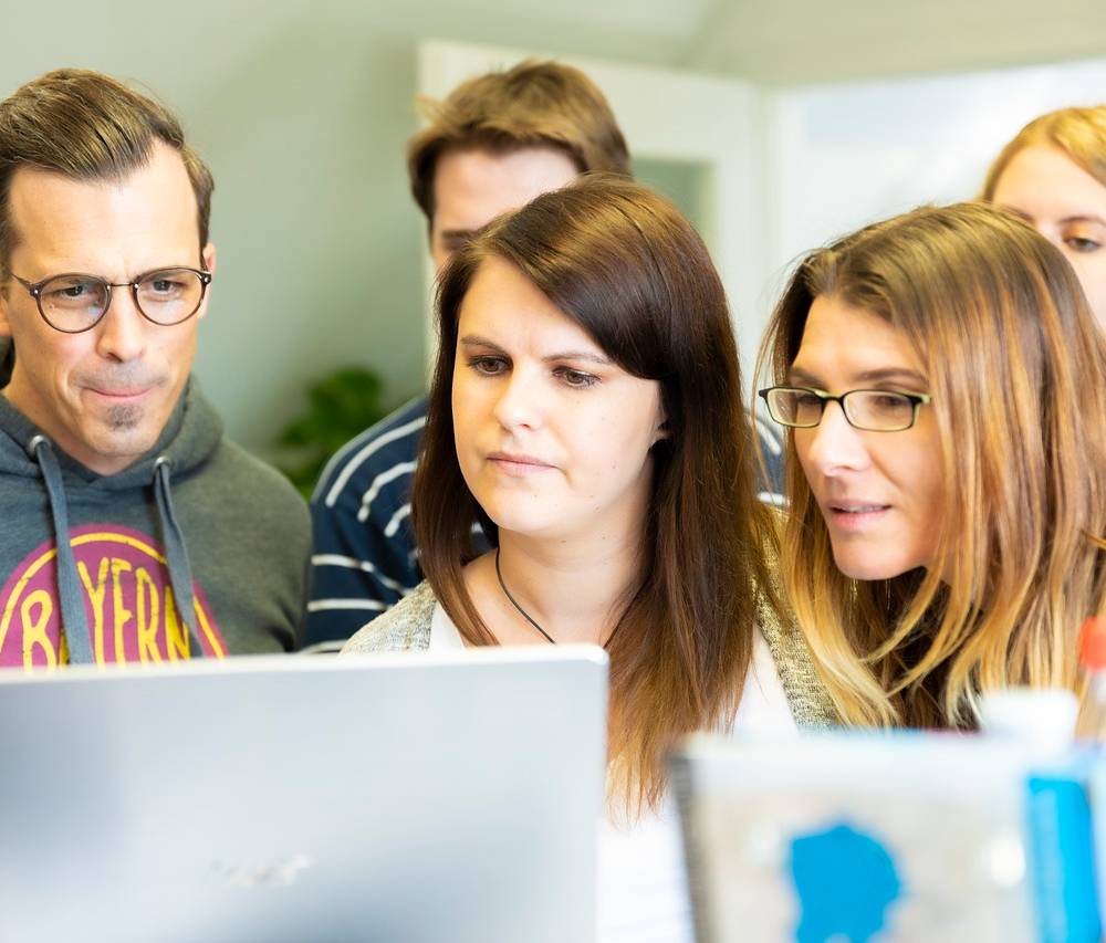 여러 명의 성인 남녀가 모여서 컴퓨터 화면을 쳐다 보고 있다.