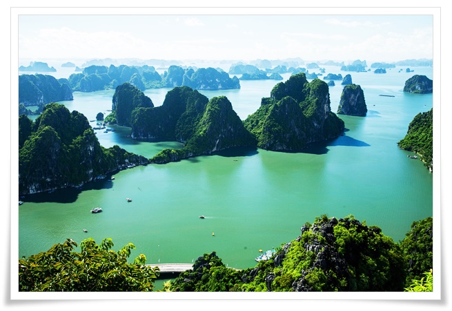 에메랄드빛 바다 위로 수많은 석회암 지형들이 솟아있고, 푸른 식생이 덮인 기암절벽들이 장관을 이루고 있습니다. 잔잔한 바다 위로 몇 척의 관광선들이 떠있으며, 수평선 너머로는 안개에 쌓인 듯한 카르스트 봉우리들이 끝없이 이어져 신비로운 분위기를 자아냅니다.