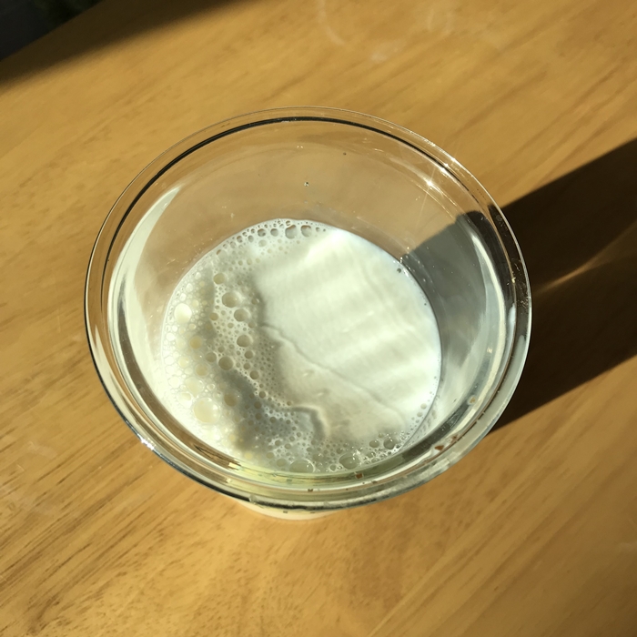 위에서 내려다본 유리컵 속 믈레코비타 갓밀크. 실내 자연광에 반사되는 우유의 질감과 기포가 생생하게 담겨 있다.