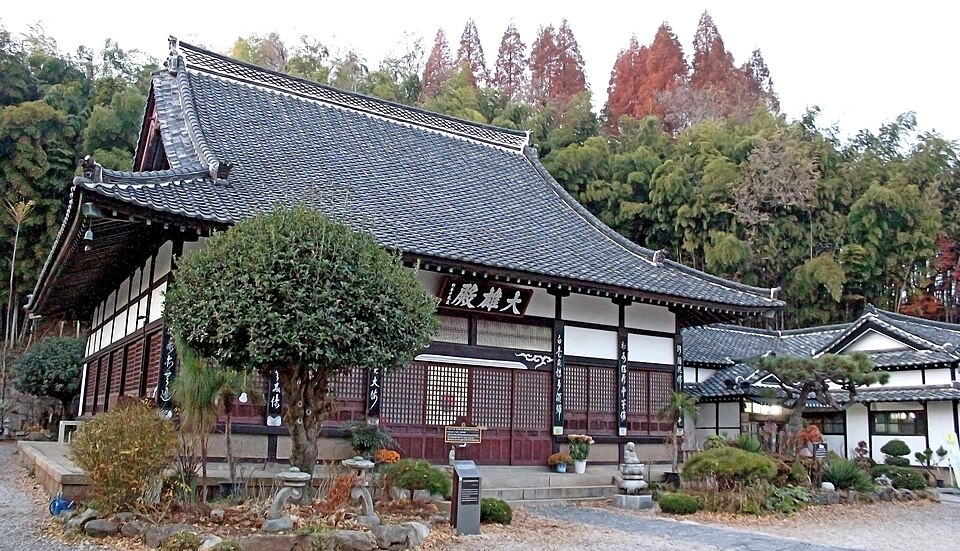 Dongguksa’s main hall has a broad tiled roof, dark wooden beams and white walls, with a small garden and autumn trees outside.