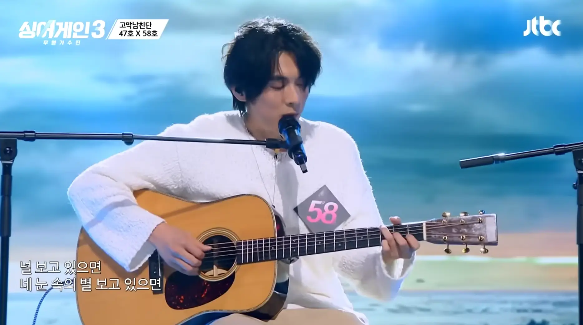 싱어게인3-
좌측 베이지색 바지에 흰색스웨터 갈색기타를 치며 의자에 앉아 스탠딩마이크에 입을 대고 노래하는 58호