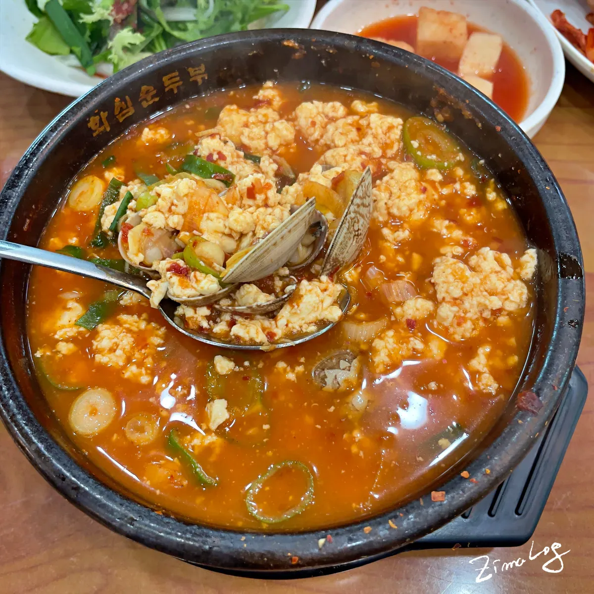 바지락 순두부찌개의 모습으로 찌개에 순두부와 바지락이 들어 있는 것을 숟가락에 떠서 있는 모습