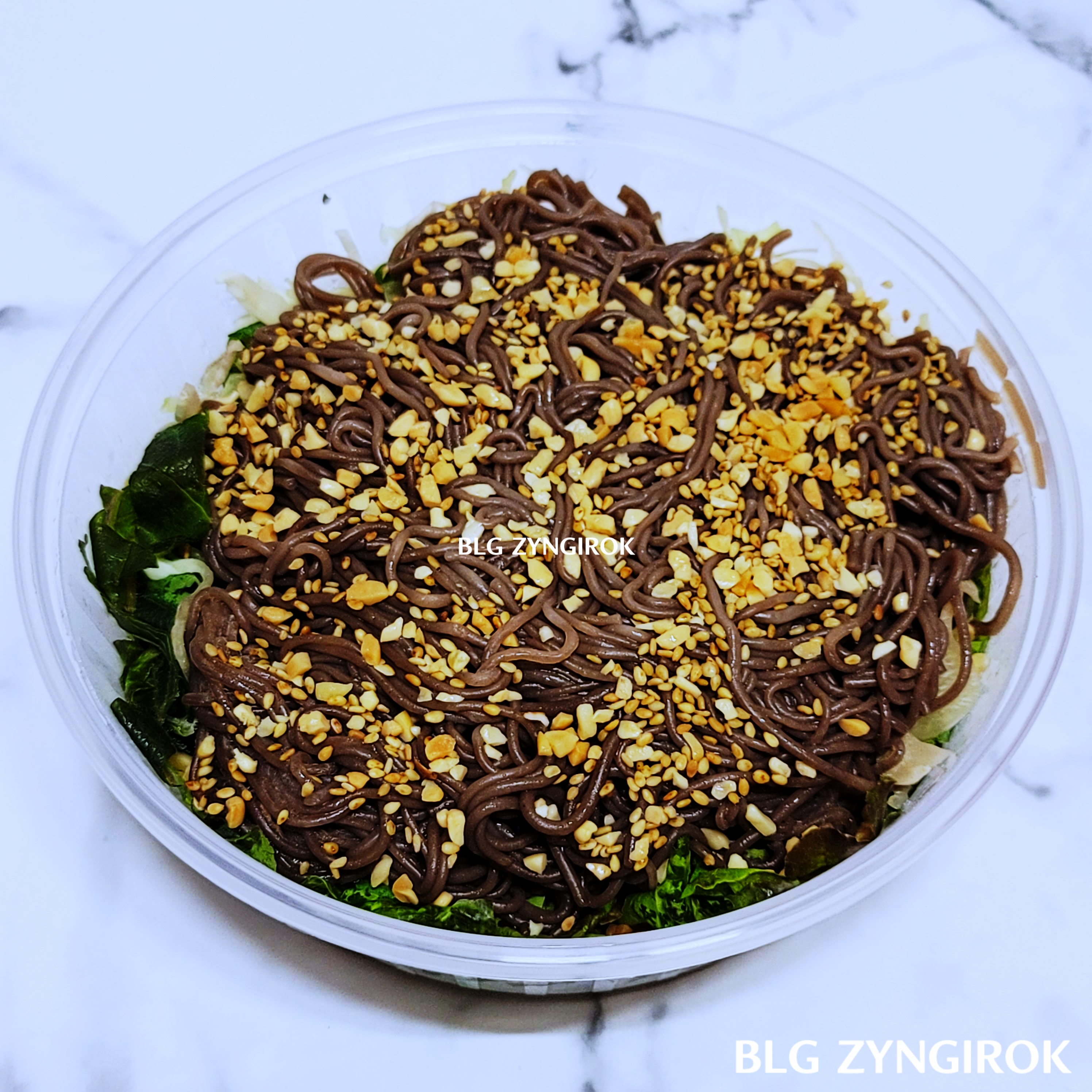 포장해온-막국수를-딱-열었을때-모습이다.-야채위에-갈색-면의-막국수가-놓여있고-그위에-견과류들이-뿌려져있다.