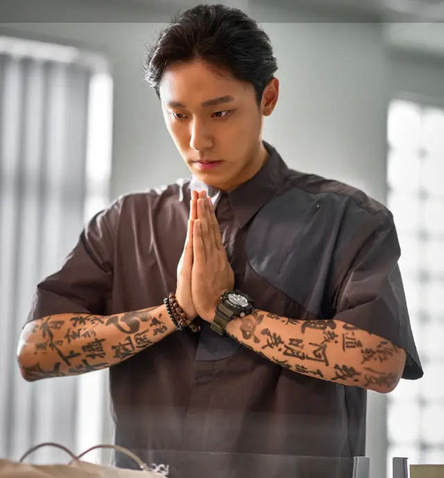 파묘- 검은반팔옷을 입고 양쪽팔에 한문을 복잡하게 써놓은 두손을 합장하고 있는 이도현