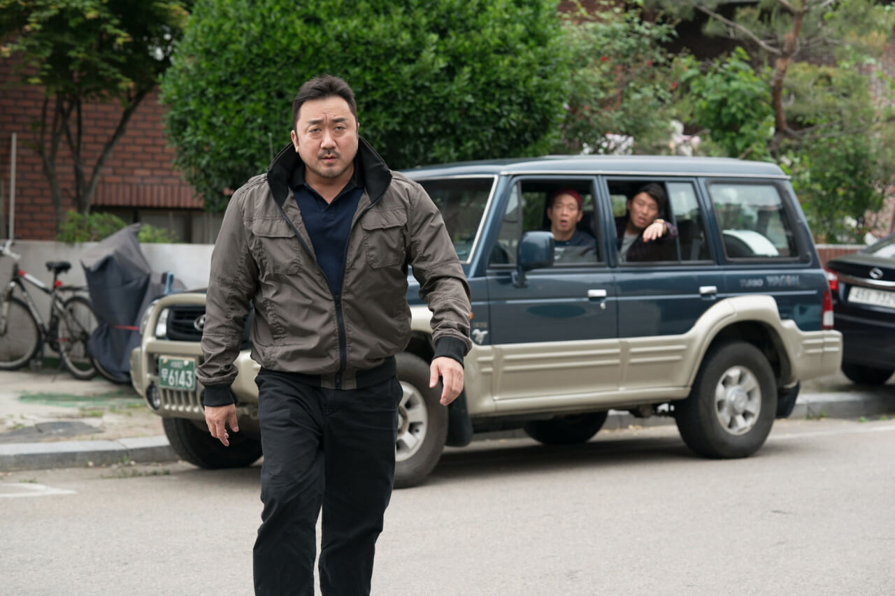 걸어가는 남자와 남자 뒤의 차량에 탄 두 남자