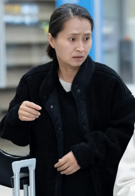 어느 실내를 배경으로 새치가 있는 단말머리에 검은 코트를 입고 서 있는 드라마 7인의 탈출의 윤지숙 캐릭터