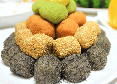 하얀 접시 위에 떡들이 가득하다. 검정 떡, 개소금덕, 인절미, 녹색 떡이 있다.