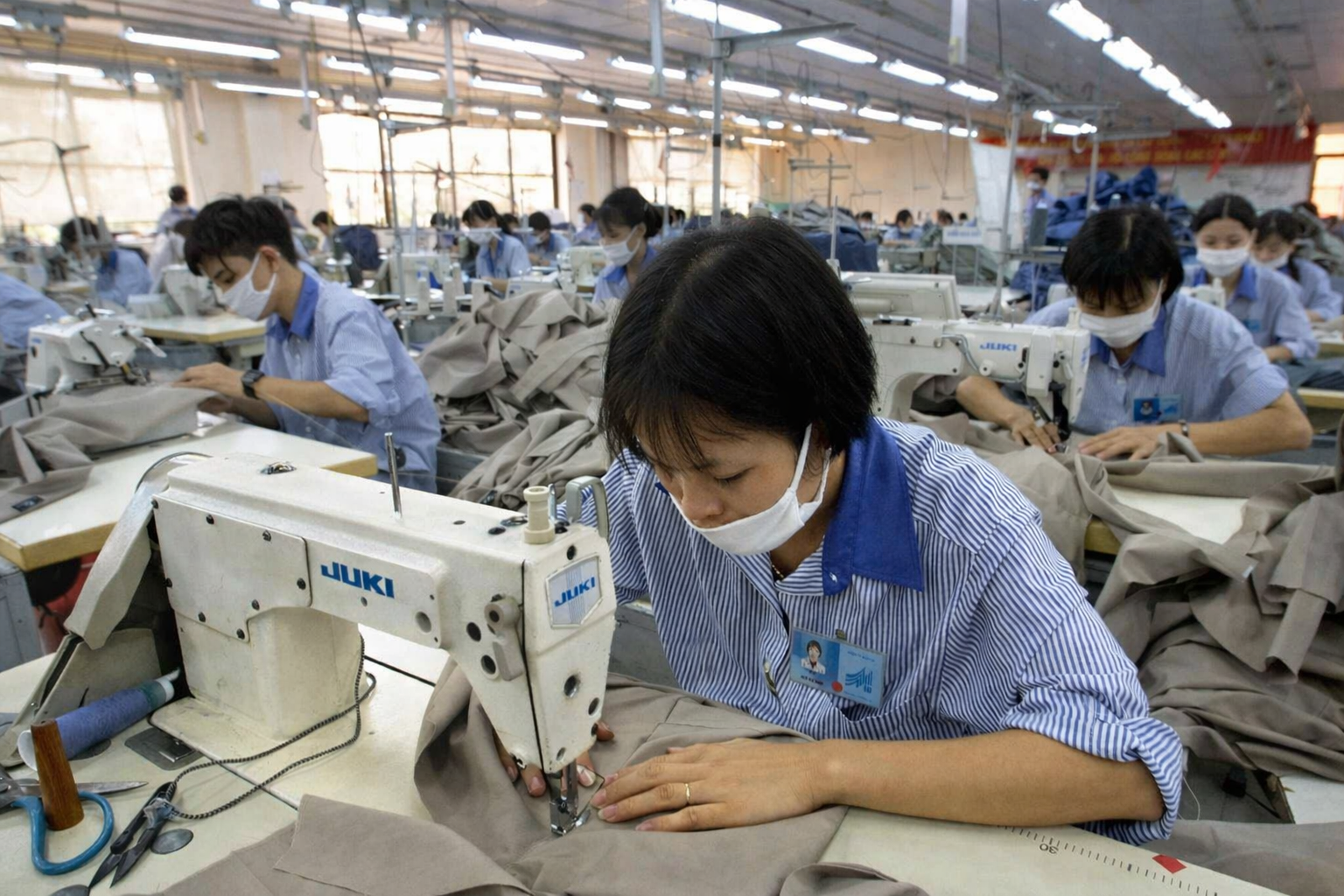 베트남 의류 공장에서 작업자가 재봉기에 앉아 천을 집중해 봉제하는 현장 모습