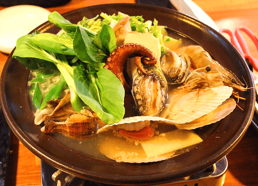 고동색 냄비에 해물탕이 가득하다. 청경채, 문어, 전복, 새우와 국물이 수북하다.