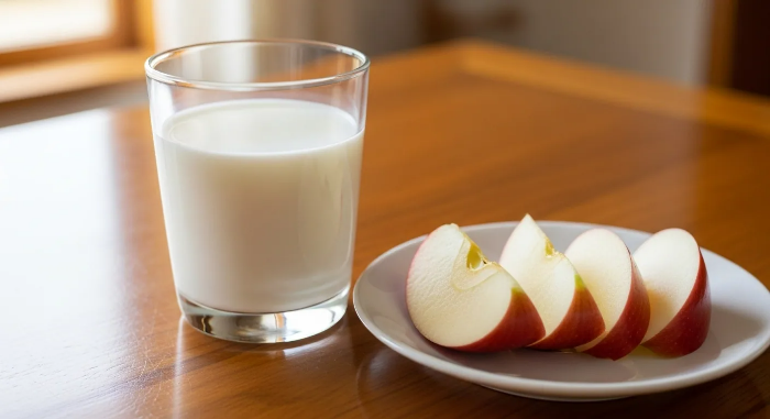 식탁 위에 우유 한잔과 사과 4조각 접시가 놓여 있음