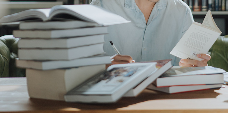 책들이 쌓여있고 공부를 하는 남자가 있다