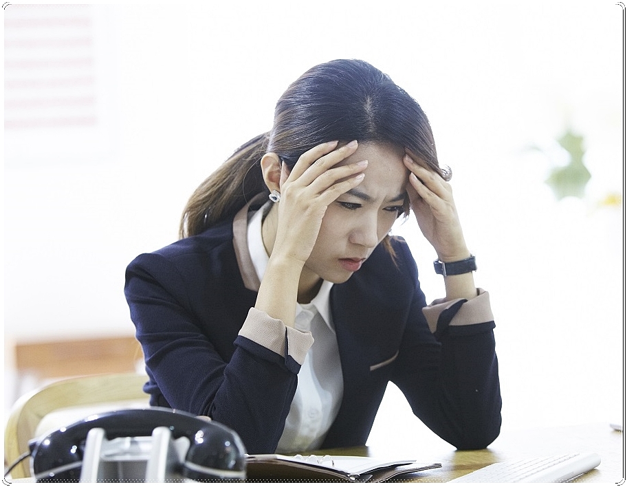 관자놀이 부위를 두 손으로 감싼 채 다소 힘겨운 표정을 짓고 있는 여성 직장인의 모습