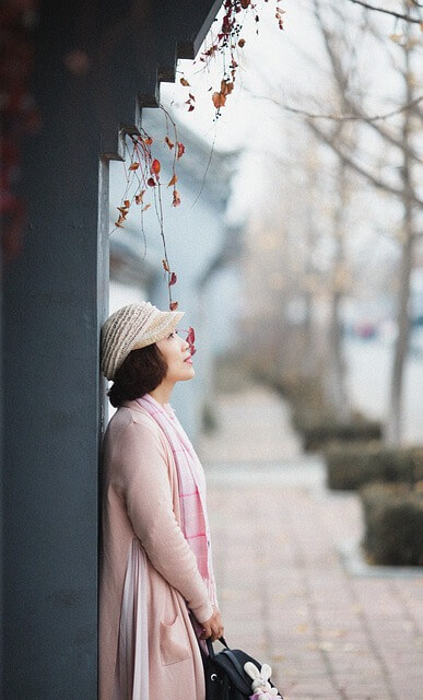 “낙엽 떨어진 거리에서 분홍빛 코트를 입고 벽에 기대어 미소 짓는 여성의 따뜻한 가을 감성”