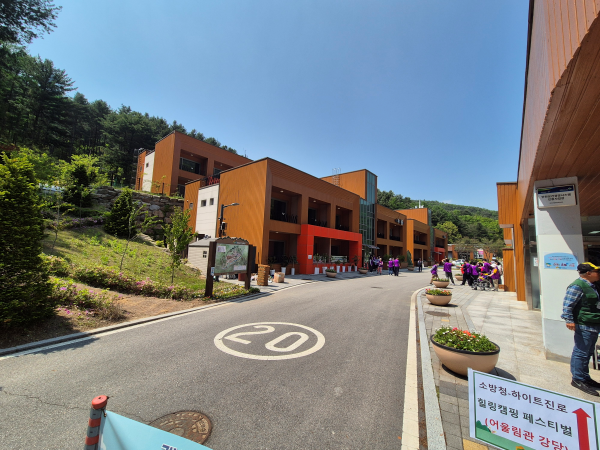 국립춘천숲체원 내 건물들과 잘 정돈된 도로, '소방청&middot;하이트진로 힐링캠핑 페스티벌' 안내판