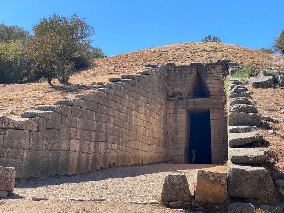 언덕에 위치한 고대 미케네 툴로스 무덤의 입구. 두꺼운 석재로 쌓은 통로와 중앙 사각 출입구, 위쪽 삼각형 창이 특징이다.