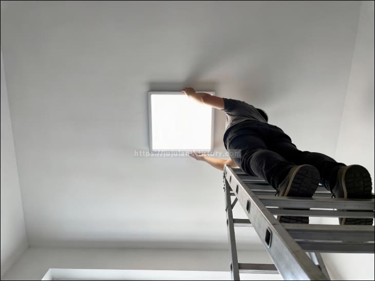 사다리-위에-올라간-사람이-양손으로-사각-LED-조명을-고정하고-있다.