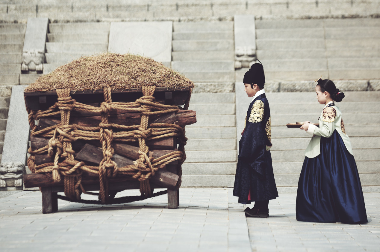 어린 사도세자가 뒤주 앞에 서 있고 옆에 여자아이가 쟁반을 들고 서 있는 장면, 뒤주의 묵직한 존재감이 화면 왼쪽을 가득 채운다