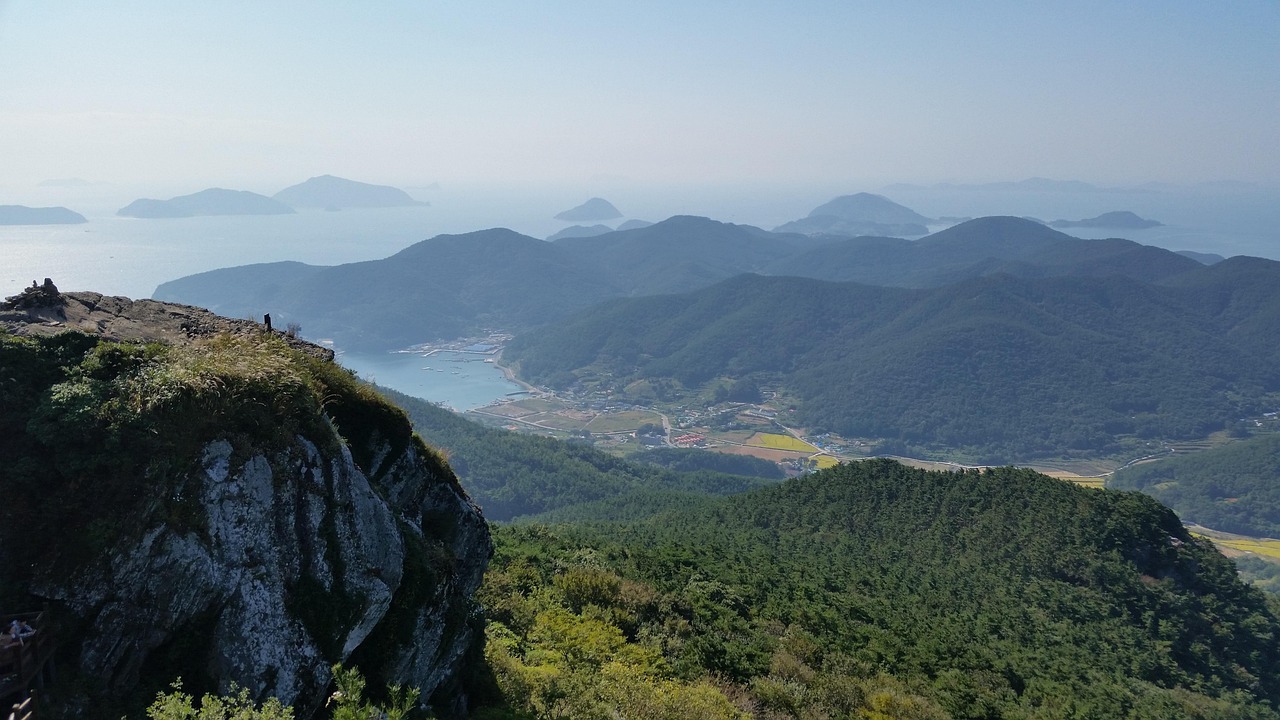 경남 통영 미륵산 정상에서 바라본 파노라마 뷰. 푸른 산맥과 바다, 섬들이 어우러진 절경이 펼쳐지며, 아래로는 마을과 항구가 보인다