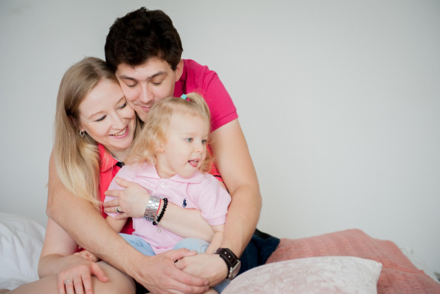 미소 지으며 아이를 감싸 안고 있는 부모의 모습