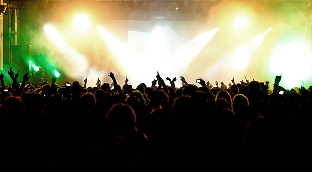 밝은 조명이 무대를 비추고 많은 사람들이 모여서 손을들고 있는 사진입니다.