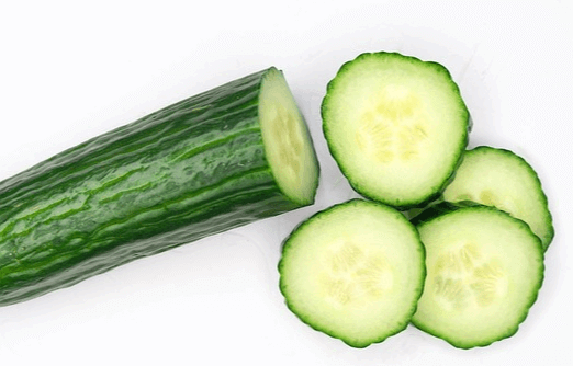 초록색 오이 반개가 있고 왼쪽에는 칼로 자른 오이 슬라이스 4조각이 있다.