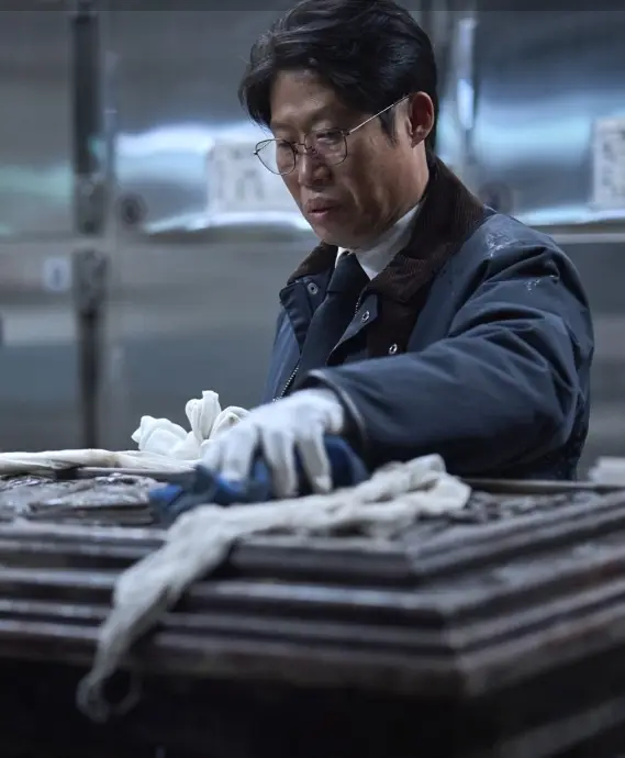 파묘- 흰색 끈으로 둘러싸인 관을 흰장갑을 끼고 닦고있는 유해진