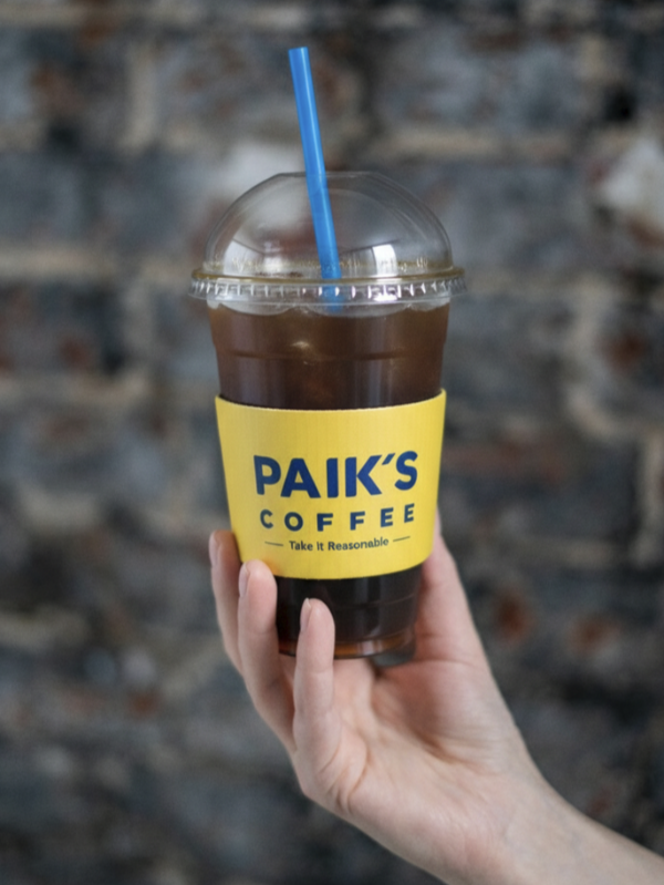 검은 돌벽 앞에 노란색 백다방 아이스 아메리카노를 들고 있는 모습