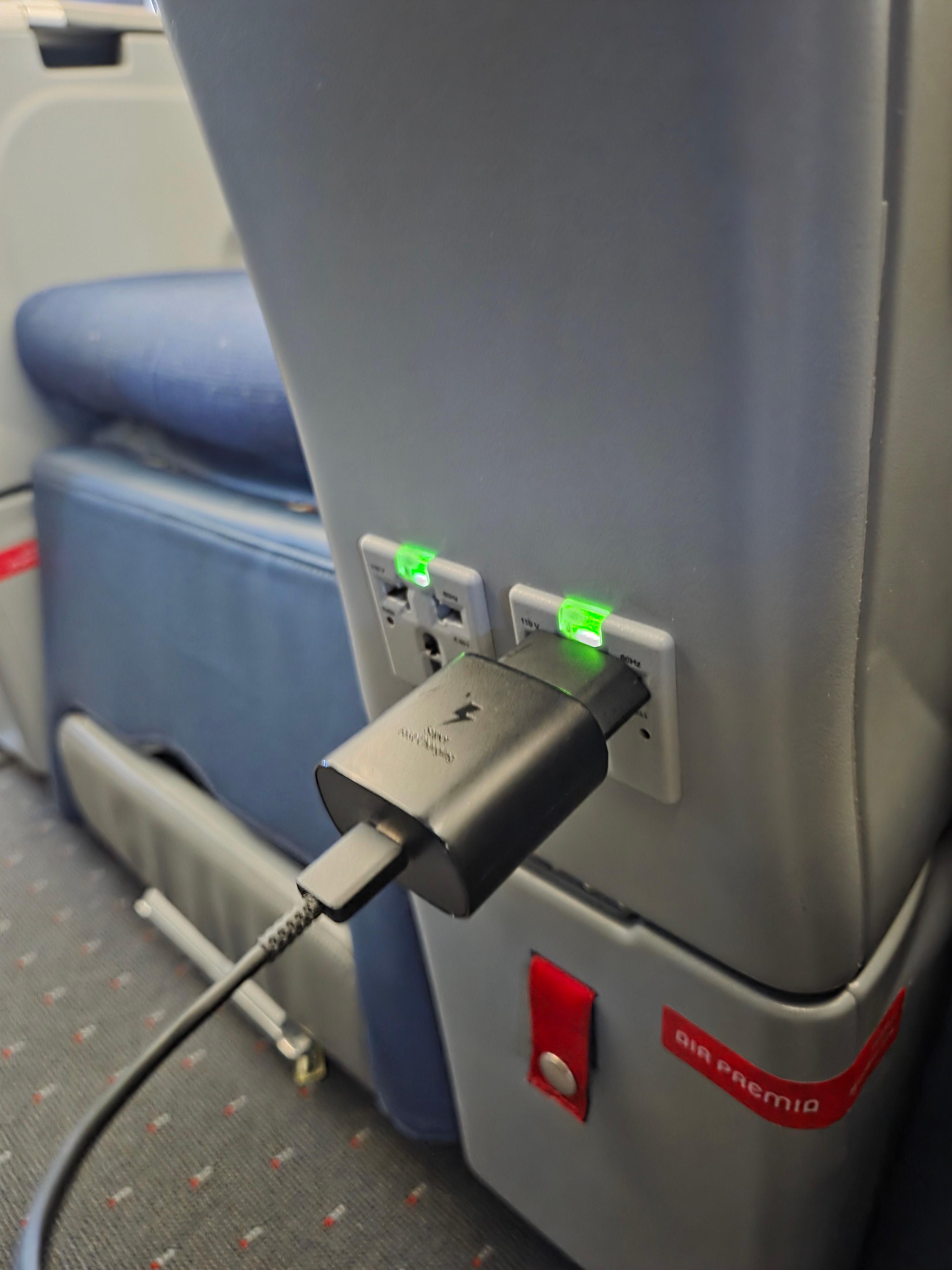 좌석 하단에 설치된 에어프레미아 전원 콘센트와 충전 중인 어댑터 모습