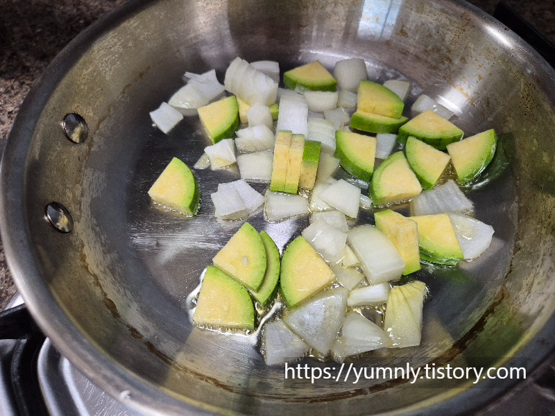 Sautéing diced zucchini and onions in olive oil in a frying pan for a healthy pasta base.