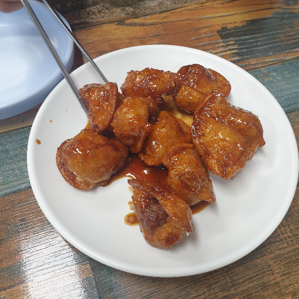 붉은 빛이 도는 양념 만두, 젓가락으로 만두 하나를 집고 있다.