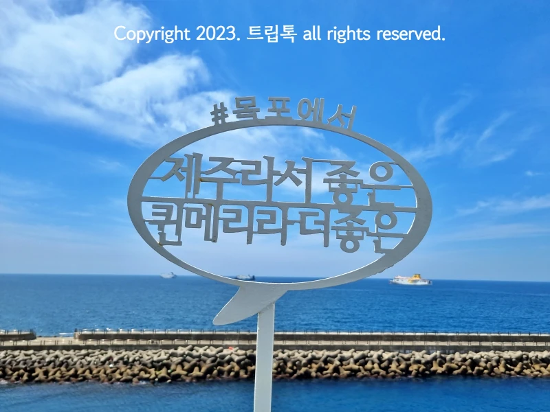 제주라서 좋은 퀸케리라 더좋은 이라고 적힌 팻말과 푸른 바다와 하늘