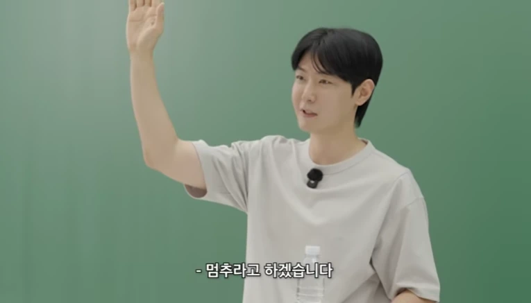 초록색 배경의 교육 영상에서 남성이 손을 들어 올리며 멈추라고 하겠습니다라고 말하는 장면