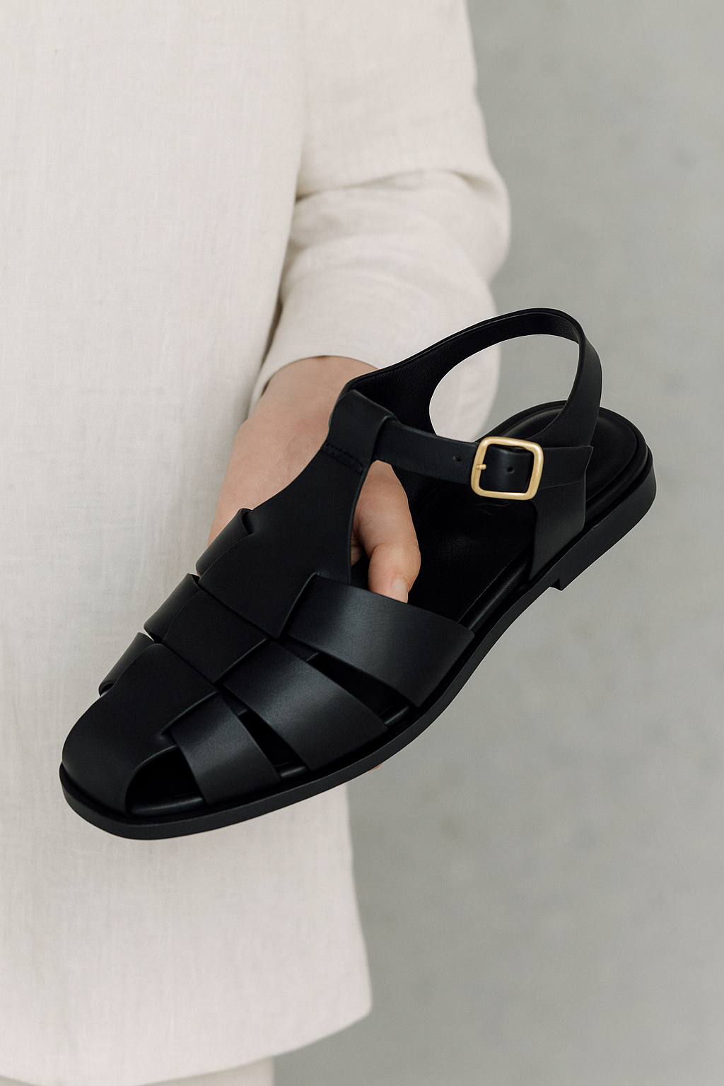 손에 들고 있는 쿠에른 샌들, 골드 버클과 가죽 질감 강조