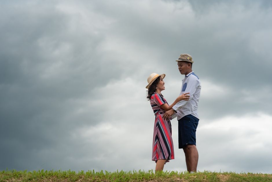 Couple standing in embrace on a grassy hill against a dramatic cloudy sky, expressing love.