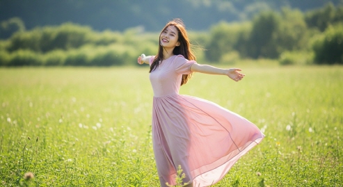 바람 부는 여름 들판에서 팔 벌려 선 젊은 여성