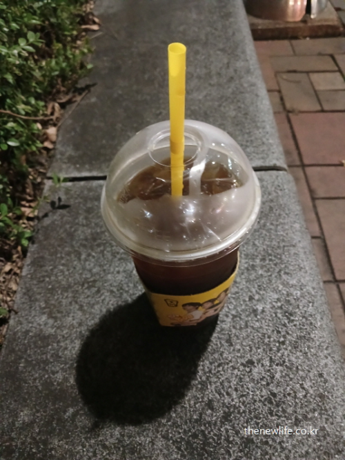 밤에 벤치 위에 놓인 아이스커피 컵 실사 사진, 공복 커피 습관이 위장과 건강에 부담을 줄 수 있음을 상징적으로 표현