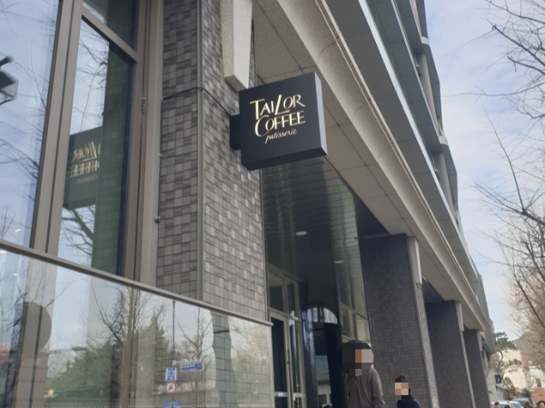 작은 테일러 커피 돌출 간판이 보이고 카페로 2명의 연인이 들어서고 있다.