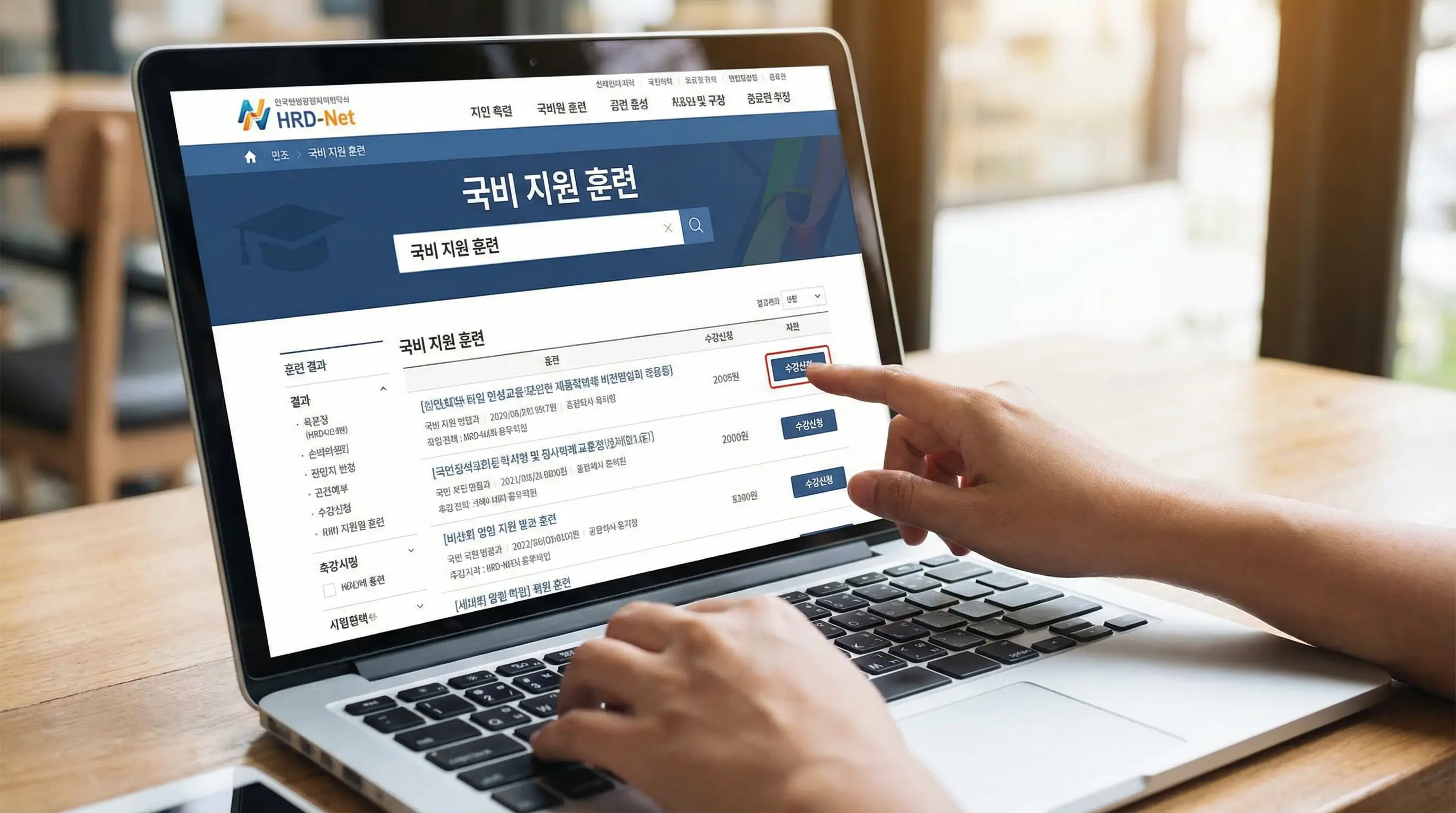 노트북으로 HRD-Net 사이트에 접속하여 국비 지원 훈련 과정을 검색하고 신청하는 손과 화면 클로즈업