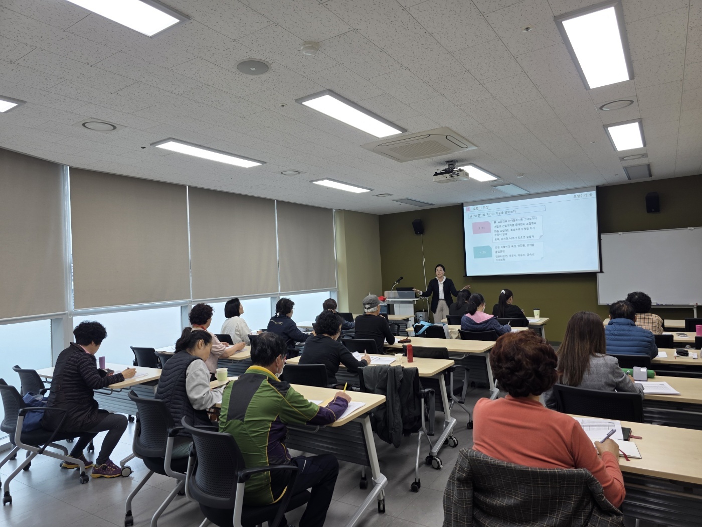 “모라평생교육원 강의실에서 오행심리 수업 중인 모습. 강사가 프로젝터를 이용해 설명하고, 수강생들은 열심히 필기하며 강의에 집중하고 있다.”