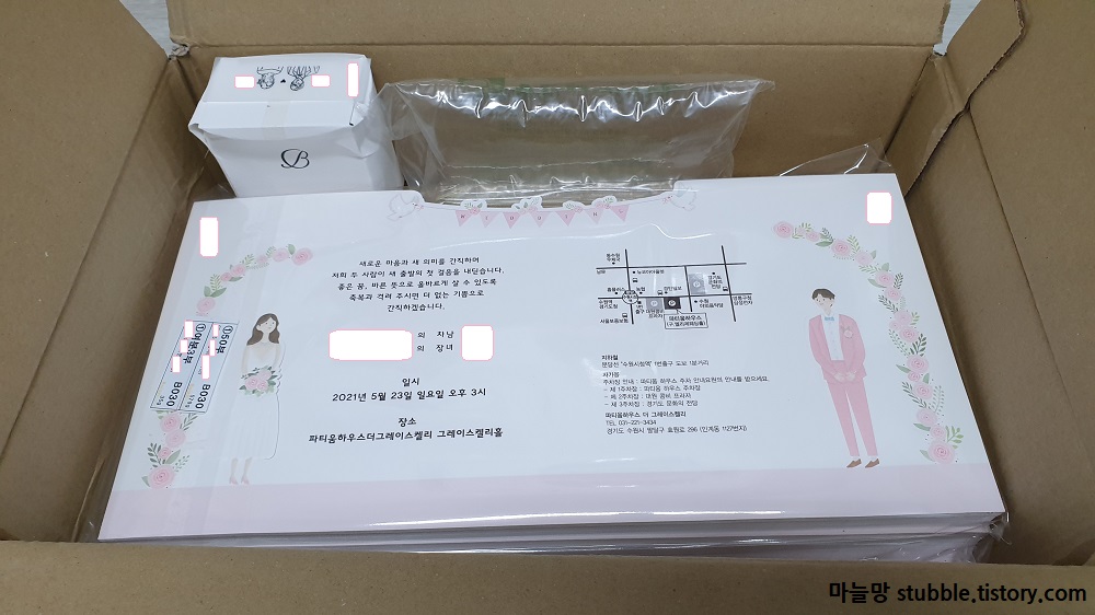 택배상자 속에 종이 청첩장이 접히지 않은 상태로 쌓여 있으며 스탬프와 청첩장을 보호하는 공기주머니가 들어있다.