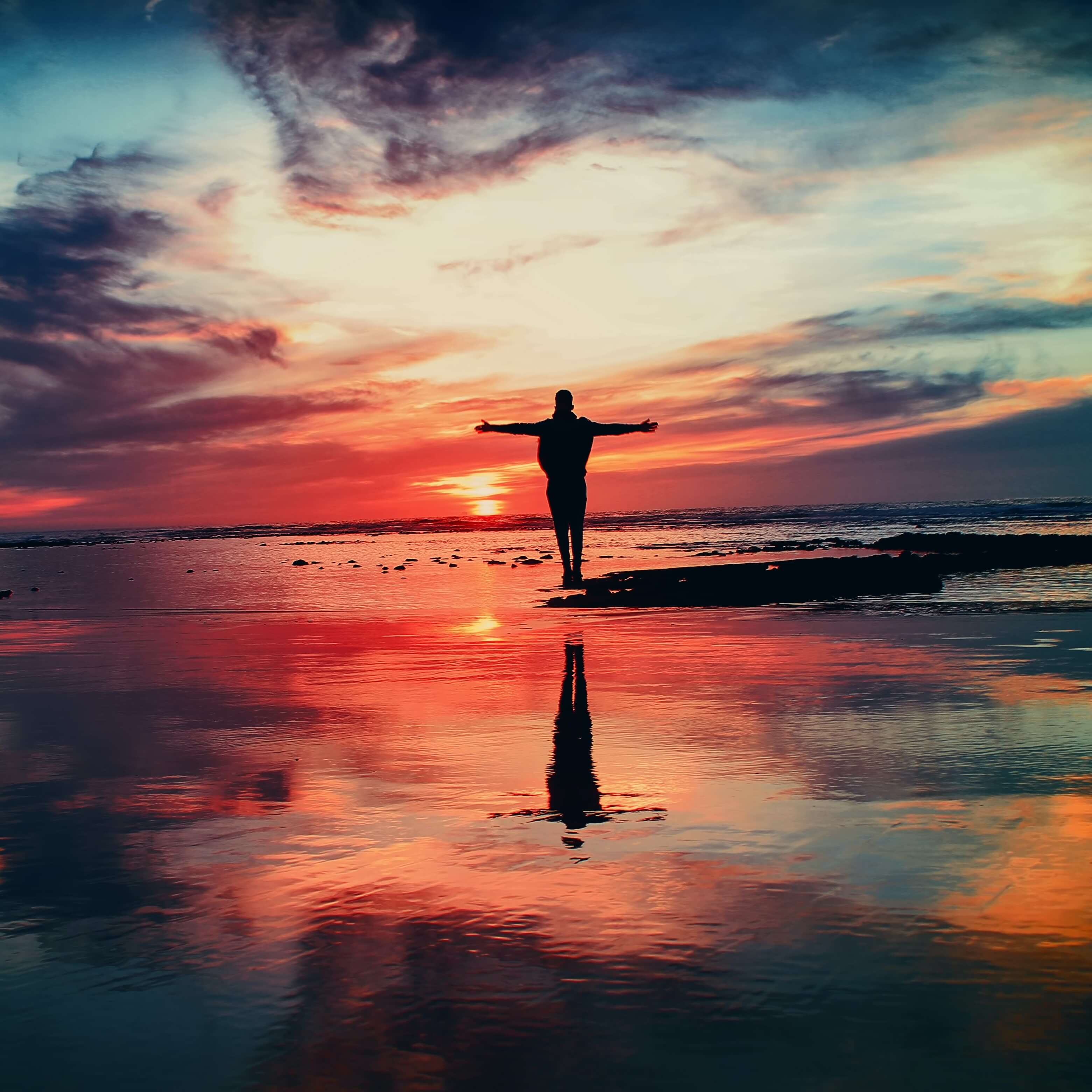 노을 지는 붉은 하늘이 바닥에 그대로 비친다. 멀리 사람이 두 팔을 벌리고 서 있다.