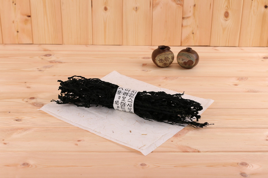 바다에서 채취를 한 미역을 깨끗하게 세척을 한 후에 바싹 말린 것을 한묶음 모은 것을 옛문자가 적힌 종이로 묶은 것을 나무 바닥 위에 종이를 깔고 그 위에 놓아두고 찍은 사진