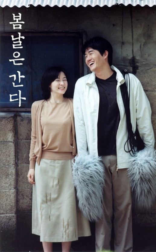 봄날은 간다 엤날 시골 벽돌 담에 기대어 한쌍의 남녀가 활짝 웃고 있다. 여자는 베이지 니트 흰스커트를입고 남자는 검정티셔츠에 흰색잠바 검정가방을메고 베이지 바지를입었고 손에는 털뭉치를 들고있다. 지방 밑에서 비를 피하는 듯한 모습이다.