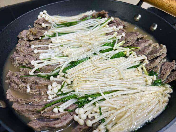 냄비 안에 고기와 야채(팽이버섯, 부추), 육수가 있는 사진이다.