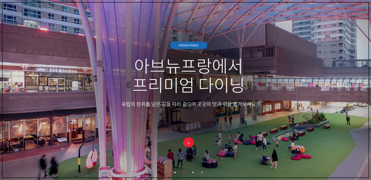 아브뉴프랑에서-프리미엄-다이닝-이라는-글씨가-정중앙에-있고-배경으로-건물과-건물사이에-넓은-푸른-잔디밭-같은-공간이-있고-그위에-빈백과--벤치가-있고-사람들이-지나가고-있는-모습-여유로운-느낌