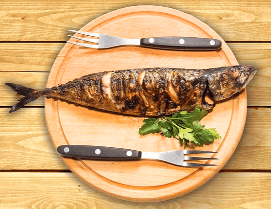 동그란 나무 접시에 잘 구운 고등어구이 한 마리가 있고 위 아래에 포크가 각각 있다.