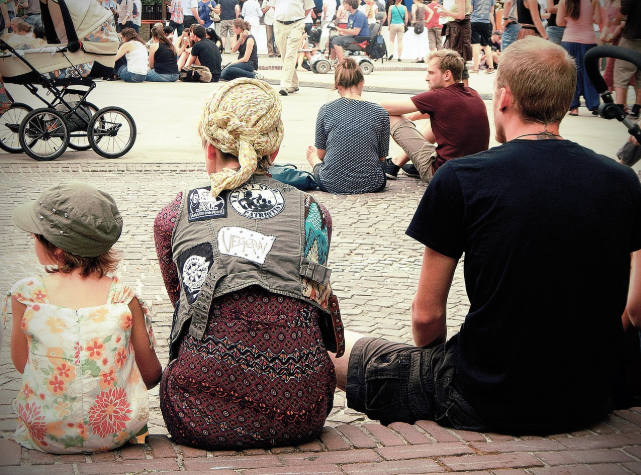 사람들 사이에서 아이와 부모가 함께 앉아 있는 모습 &ndash; 아이의 감정을 존중하며 곁을 지키는 부모의 태도를 상징적으로 보여줍니다.