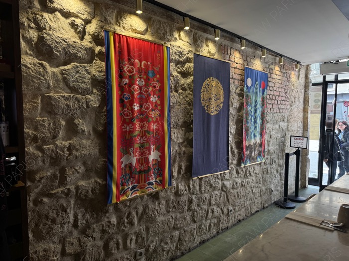 An interior stone wall decorated with traditional colorful Korean fabrics and artistic lighting inside SAMSO Paris ❘ Un mur en pierre décoré de tissus traditionnels coréens à l'intérieur de SAMSO