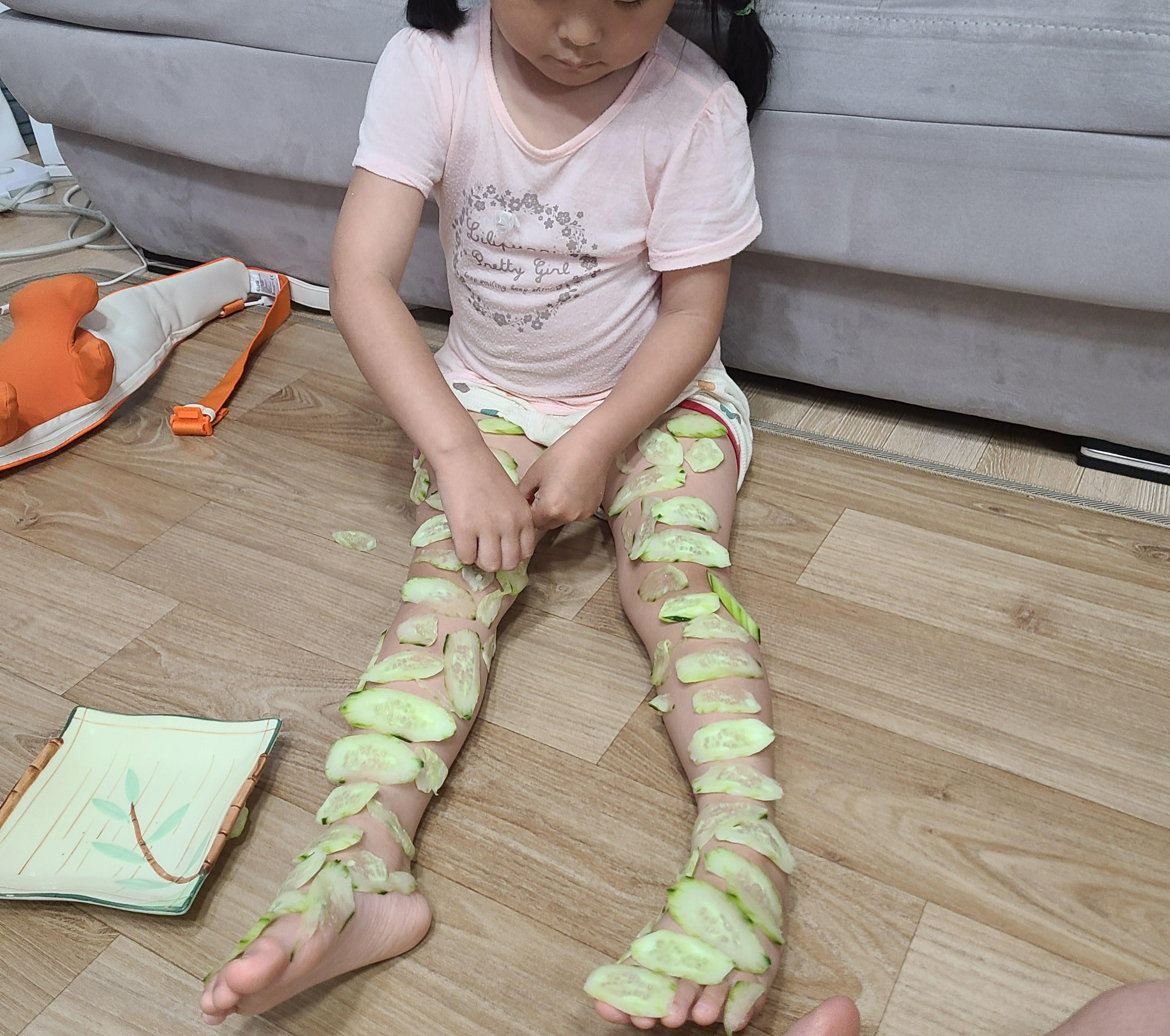 다리에 동그란 오이 조각들을 붙이고 오이 마사지를 즐기는 아이 모습